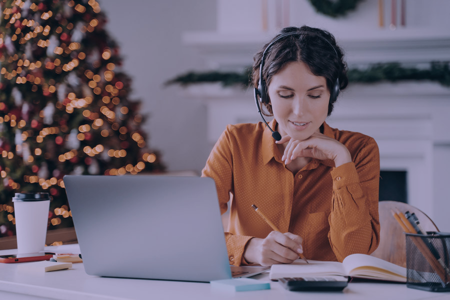 Uma mulher trabalhando de forma independente em frente a um laptop, com uma árvore de Natal visível no fundo desfocado.