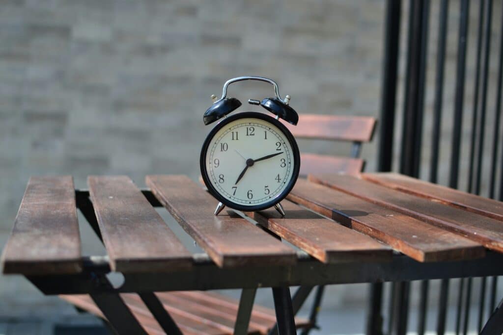 An alarm clock that can be used for time management techniques placed on a slotted wood table.