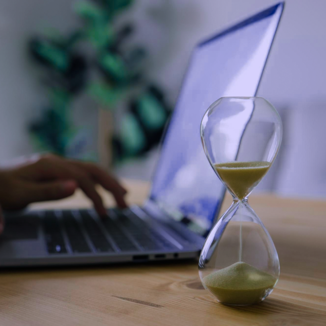 Una foto de un reloj de arena con una computadora portátil en el fondo