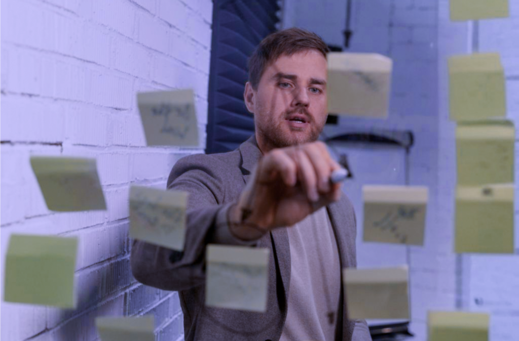 A person writing on a glass window with a marker, with many yellow sticky notes attached on that window.