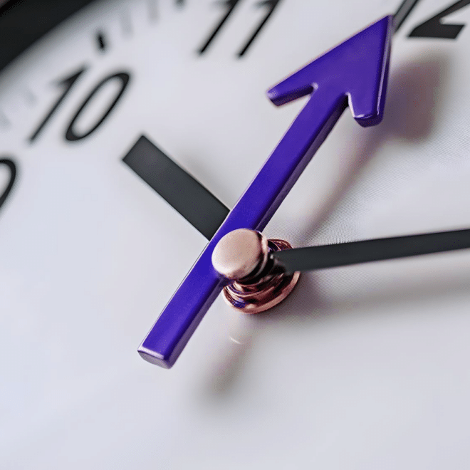 Фотография крупным планом белых часов с одной фиолетовой стрелкой и двумя черными стрелками.