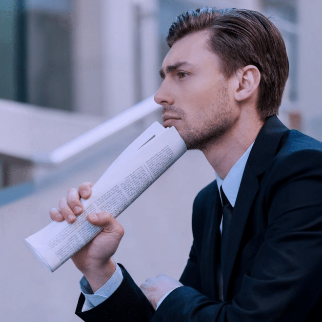A man in a suit holding a rolled newspaper up to his chin thinking about business bottlenecks
