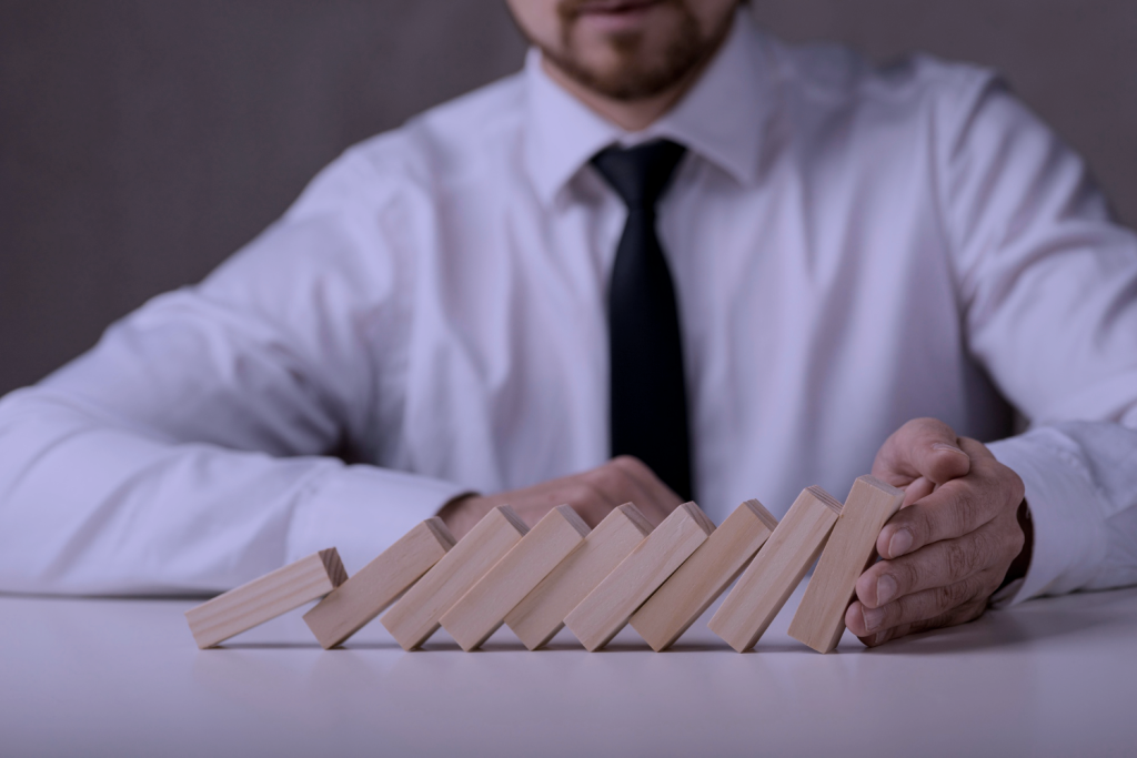 A man in a suit stopping a line of dominoes from falling over, signifying the concept of crisis management in business.