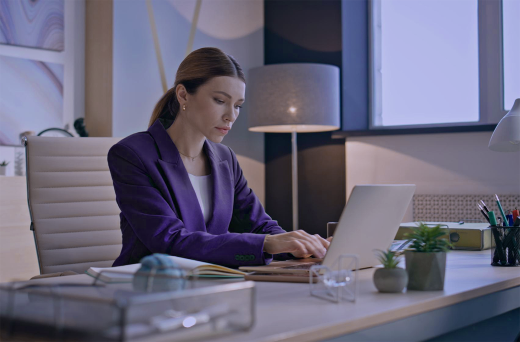 A woman in a purple coat working on establishing micro habits on a laptop.