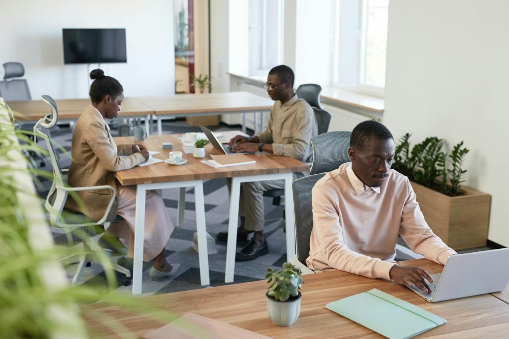 Diverse group working in a modern office setting with laptops and wooden desks.
