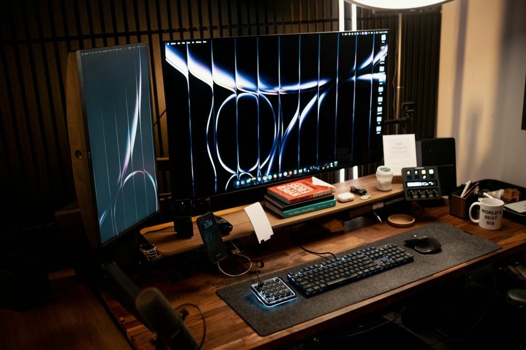 A stylish and modern home office setup featuring dual monitors, books, keyboard, and decor on a wooden desk.