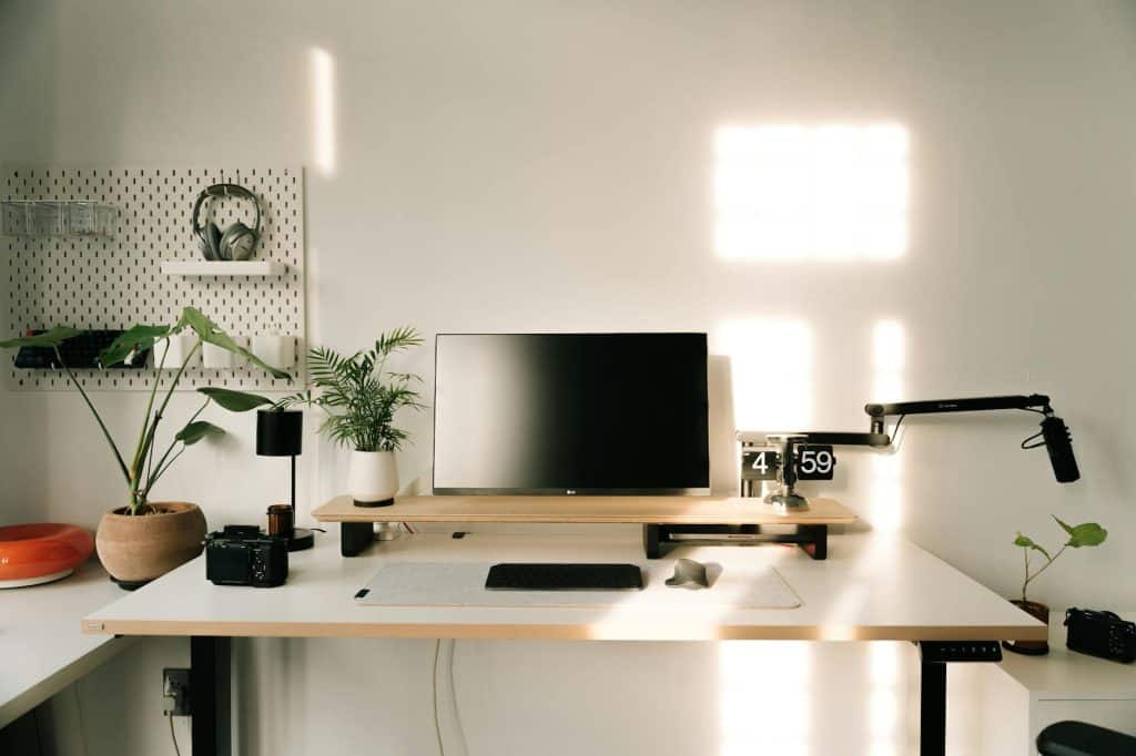 A clean and minimalist home office setup with plants, monitor, and microphone.