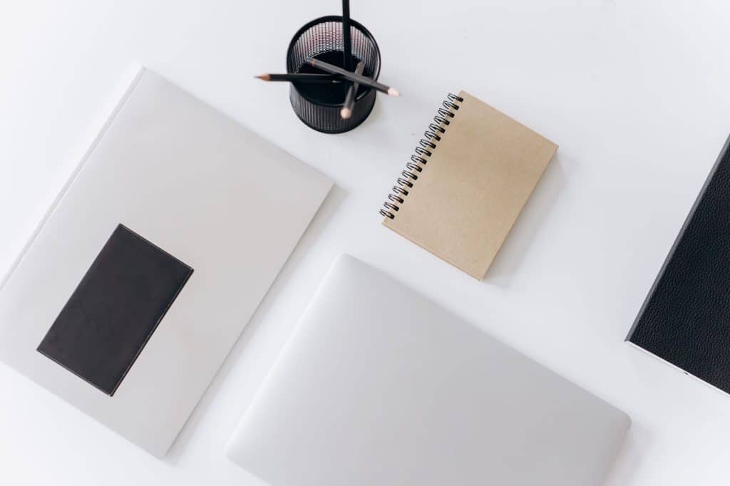 Top view of modern laptop with notebooks and cup of pencils composed on white table in office