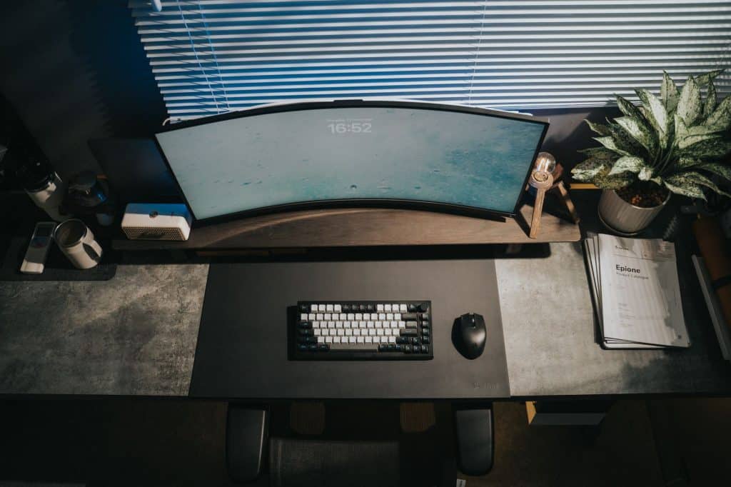 Stylish home office setup with a curved monitor, keyboard, and a lush succulent for a contemporary workspace.