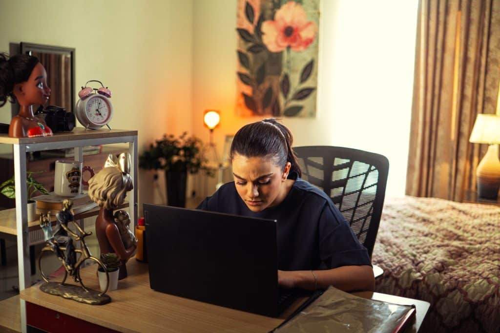 A woman intensely working on a laptop at her home office desk, surrounded by decor.